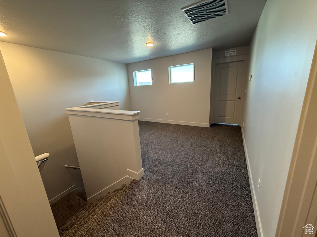 Corridor with an upstairs landing, a textured ceiling, baseboards, and dark colored carpet