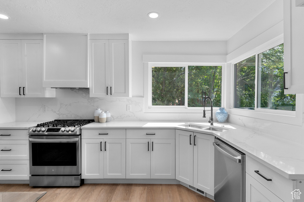 Kitchen featuring stainless steel appliances, a sink, white cabinets, decorative backsplash, and light stone counters