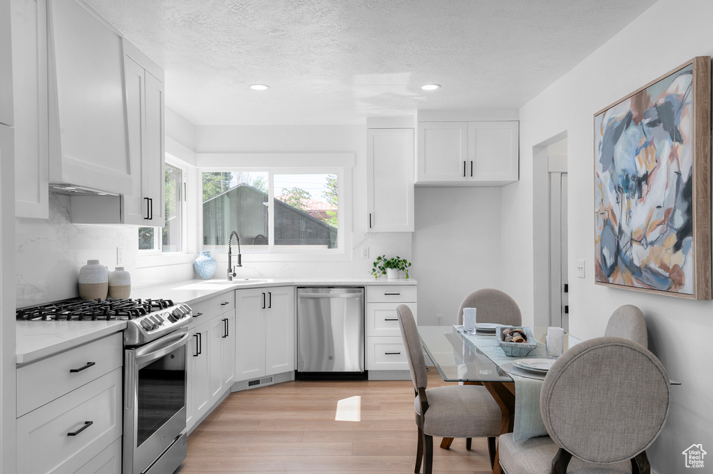 Kitchen with appliances with stainless steel finishes, a sink, light wood finished floors, white cabinets, and a textured ceiling