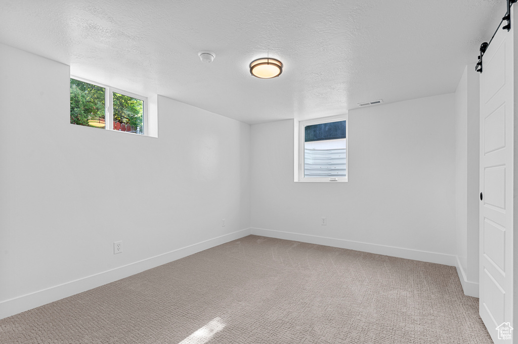 Unfurnished room featuring a barn door, carpet, baseboards, and a textured ceiling