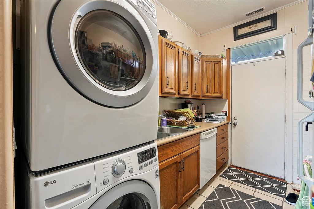 Laundry room with stacked washer and clothes dryer, ornamental molding, light tile patterned floors, and cabinet space