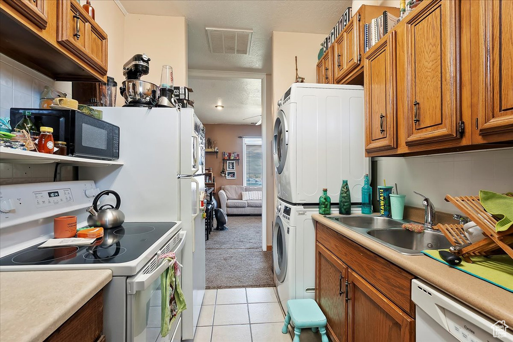 Kitchen with white appliances, stacked washer / drying machine, brown cabinets, a sink, and tasteful backsplash