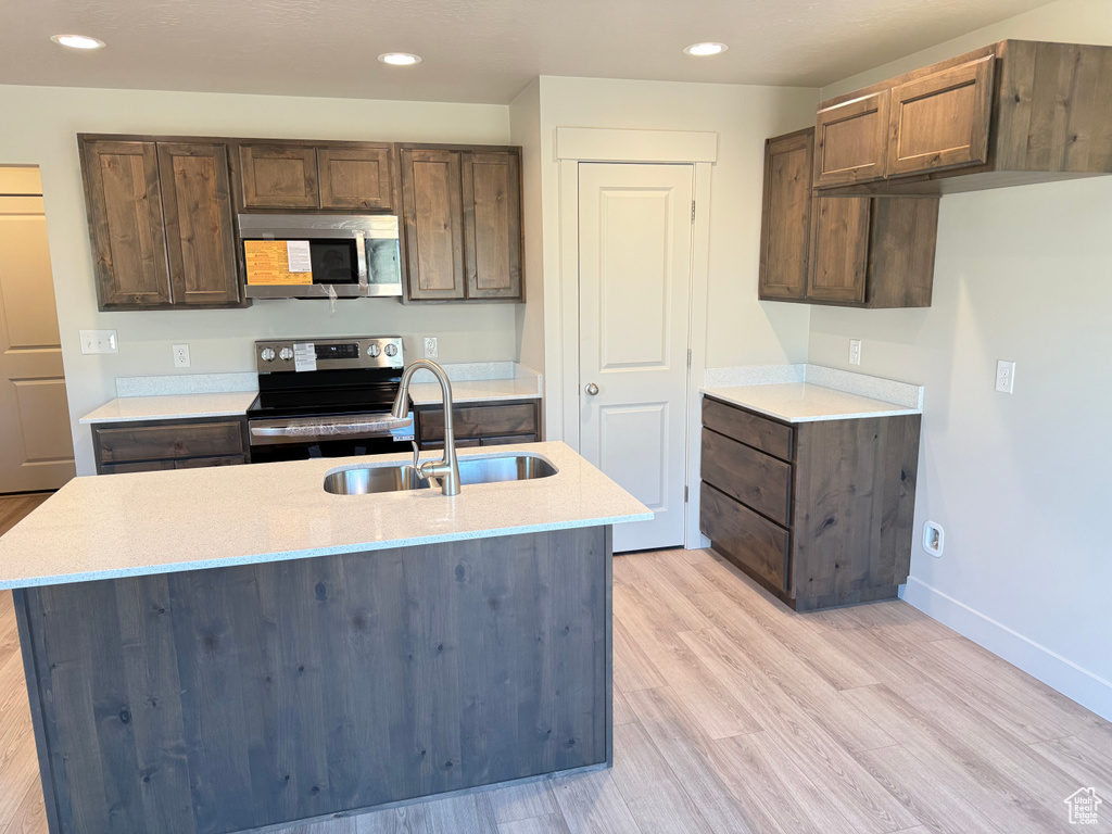 Kitchen featuring stainless steel appliances, a sink, light wood-style floors, baseboards, and light stone countertops