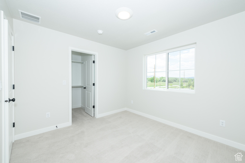 Unfurnished bedroom featuring light colored carpet, baseboards, a walk in closet, and a closet