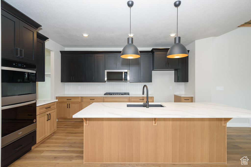 Kitchen with stainless steel appliances, a sink, light wood-style flooring, tasteful backsplash, and recessed lighting