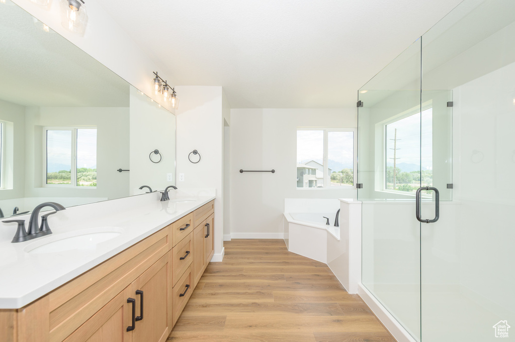 Bathroom with wood finished floors, a bath, double vanity, a shower stall, and baseboards