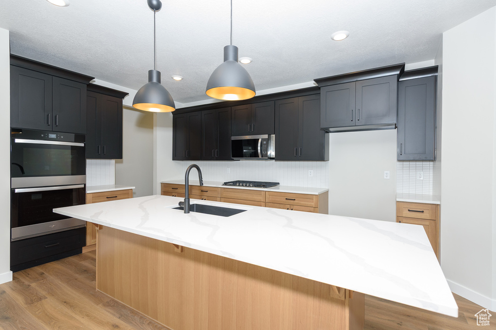 Kitchen featuring stainless steel microwave, double wall oven, decorative backsplash, a sink, and light stone countertops