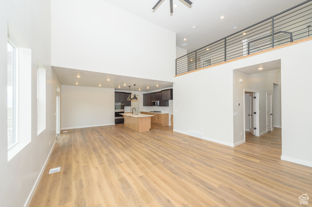 Unfurnished living room featuring a high ceiling, a sink, light wood-style flooring, baseboards, and healthy amount of natural light