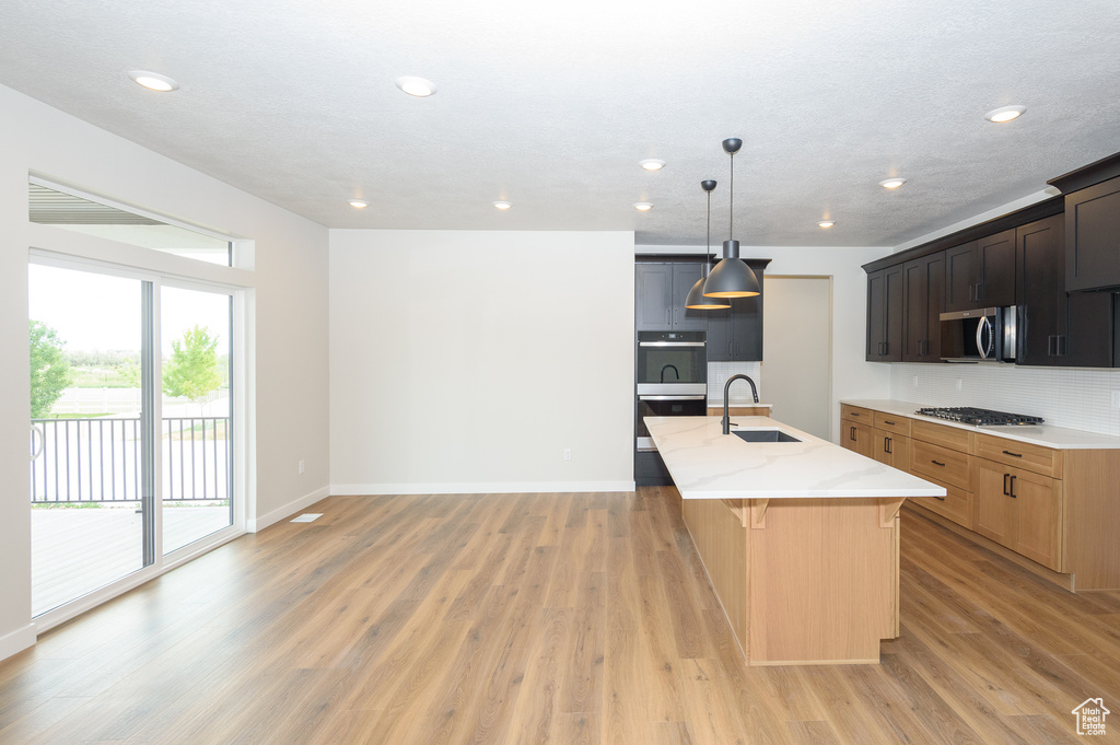 Kitchen featuring a sink, appliances with stainless steel finishes, light stone counters, light wood-type flooring, and recessed lighting