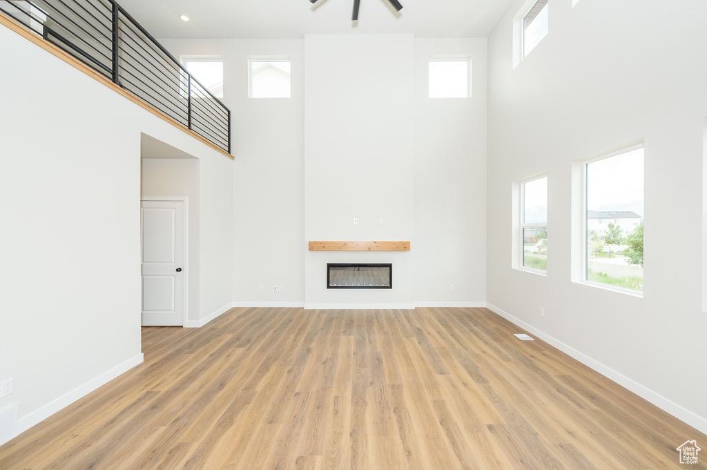 Unfurnished living room with a high ceiling, a fireplace, baseboards, and wood finished floors