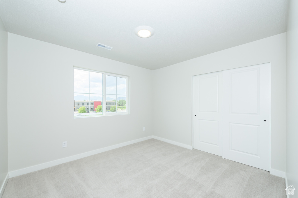 Unfurnished bedroom with light carpet, baseboards, and a closet