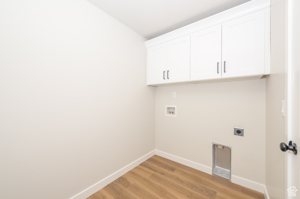 Washroom featuring electric dryer hookup, baseboards, light wood finished floors, and cabinet space