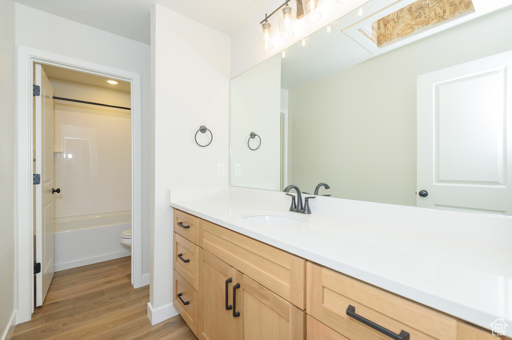 Full bath with vanity, wood finished floors, toilet, bathtub / shower combination, and baseboards