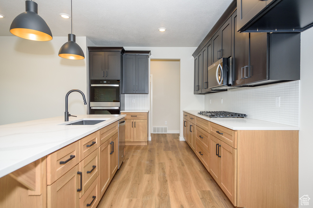 Kitchen with appliances with stainless steel finishes, a sink, light wood-style floors, light countertops, and decorative backsplash