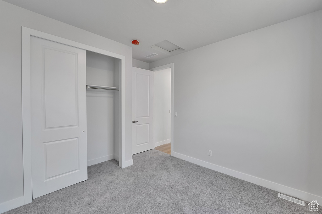 Unfurnished bedroom with carpet floors, attic access, baseboards, and a closet