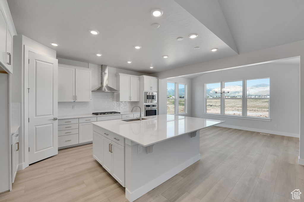 Kitchen with wall chimney range hood, a sink, appliances with stainless steel finishes, light wood-style flooring, and recessed lighting