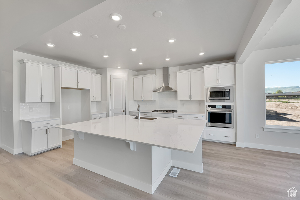 Kitchen featuring wall chimney exhaust hood, appliances with stainless steel finishes, a sink, white cabinets, and recessed lighting