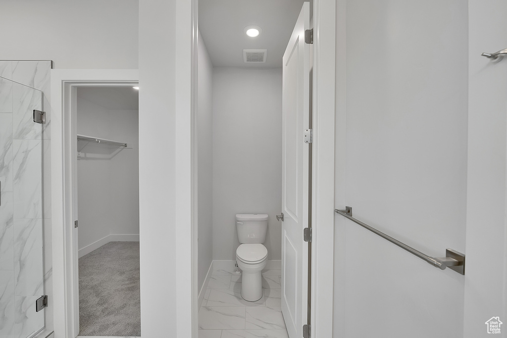 Bathroom featuring a marble finish shower, toilet, marble finish flooring, a spacious closet, and baseboards