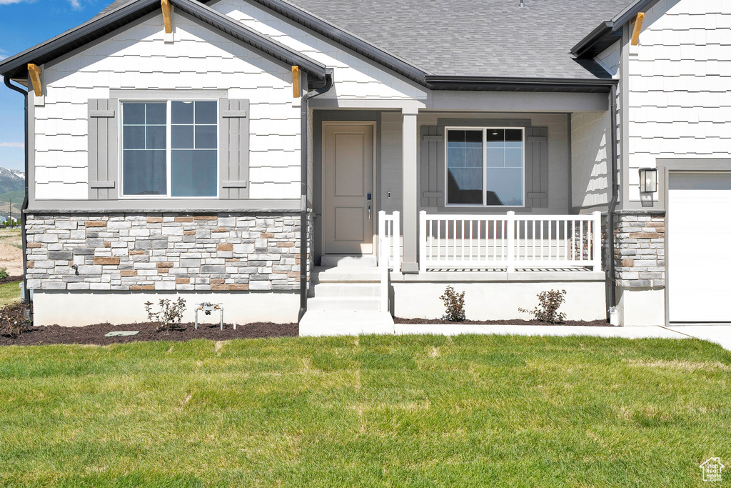 Doorway to property featuring stone siding, a porch, a garage, a yard, and roof with shingles