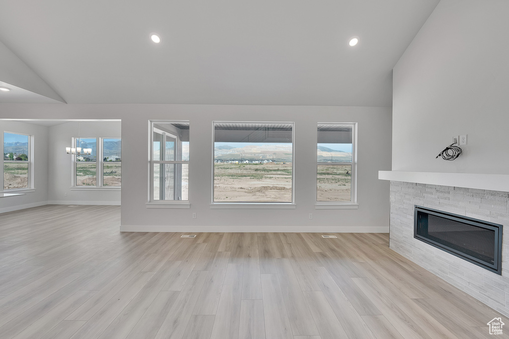 Unfurnished living room featuring lofted ceiling, a fireplace, light wood-style floors, baseboards, and recessed lighting