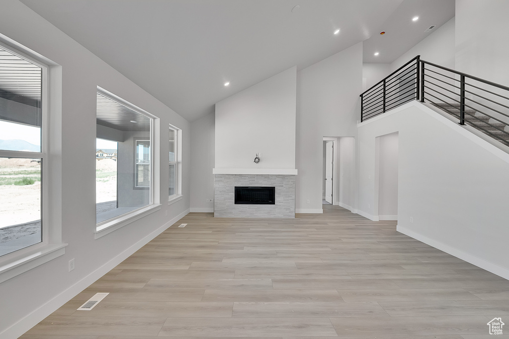Unfurnished living room with recessed lighting, light wood finished floors, a fireplace, baseboards, and high vaulted ceiling
