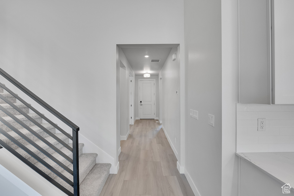 Hallway with light wood finished floors, stairway, and baseboards