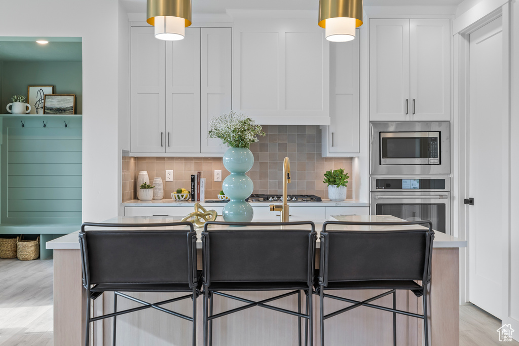 Kitchen with stainless steel appliances, white cabinetry, light countertops, decorative backsplash, and decorative light fixtures