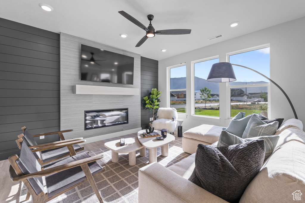 Living room with recessed lighting, a fireplace, a ceiling fan, wood walls, and wood finished floors