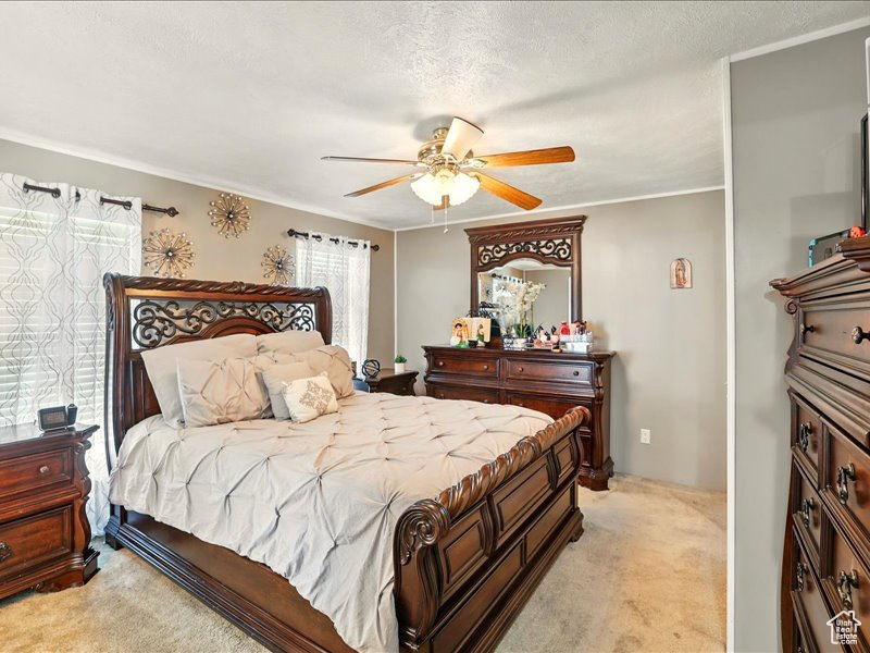 Bedroom featuring light colored carpet, ornamental molding, and ceiling fan