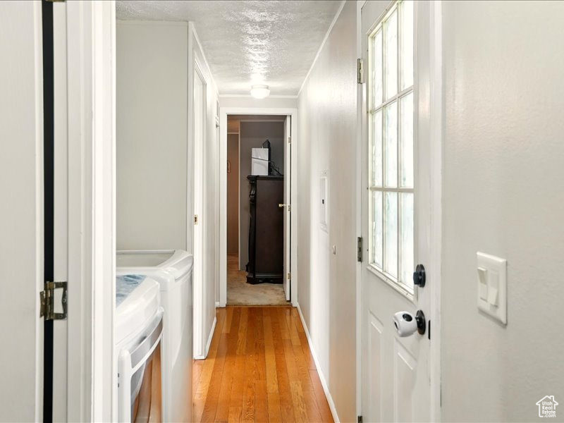 Hallway featuring independent washer and dryer, light wood finished floors, a textured ceiling, baseboards, and crown molding