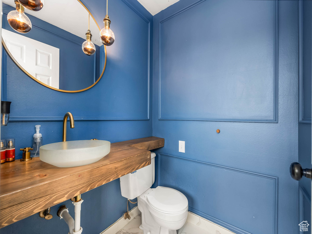 Bathroom with a sink, marble look tiles, and toilet