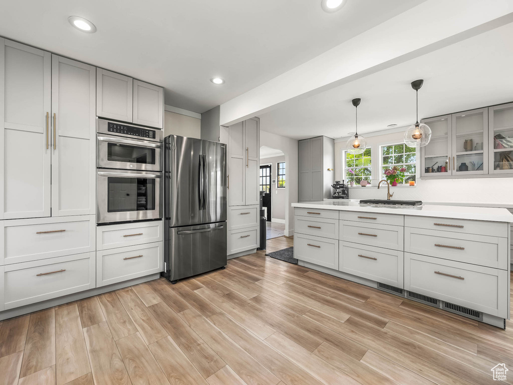 Kitchen featuring appliances with stainless steel finishes, a sink, gray cabinetry, light countertops, and light wood finished floors