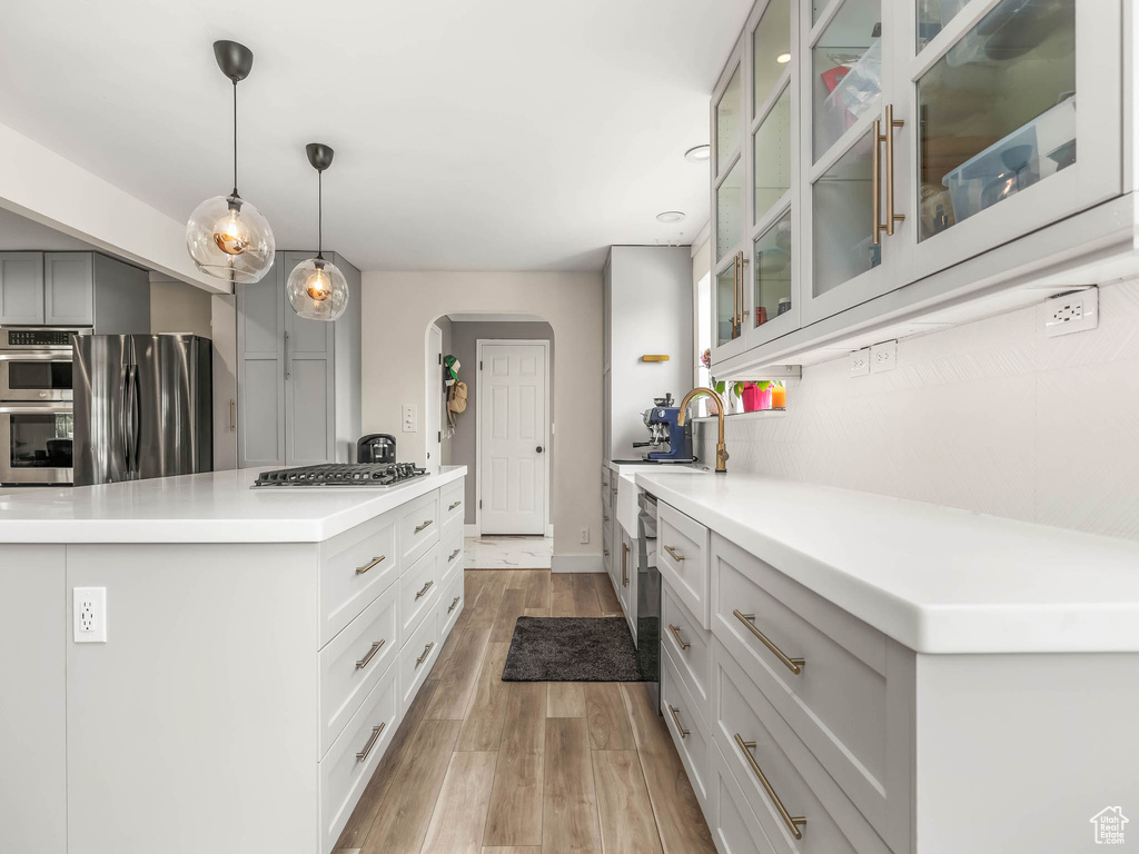 Kitchen featuring stainless steel appliances, arched walkways, light wood-style flooring, light countertops, and a kitchen island