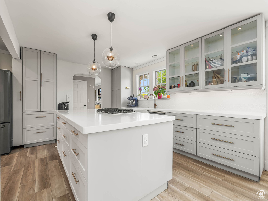 Kitchen featuring arched walkways, a kitchen island, appliances with stainless steel finishes, and light wood-style flooring