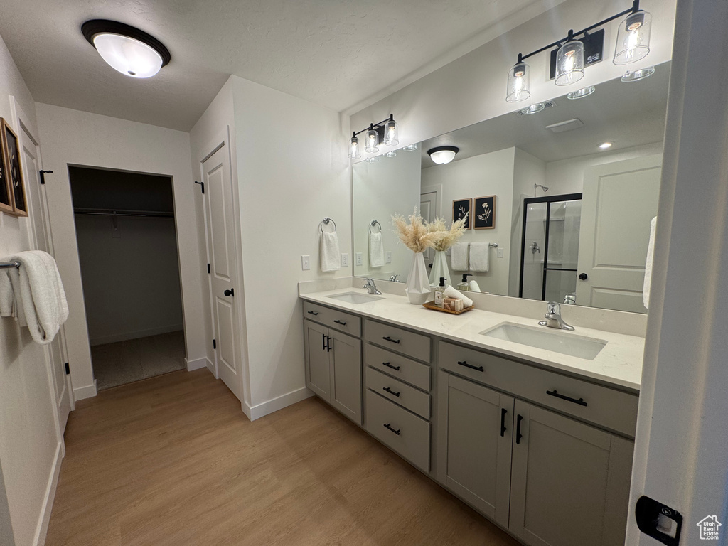 Full bath featuring a stall shower, wood finished floors, double vanity, baseboards, and a walk in closet
