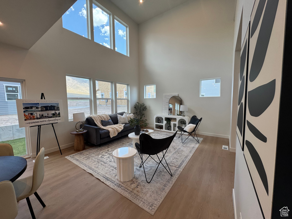 Living room with baseboards, a high ceiling, light wood-type flooring, and healthy amount of natural light