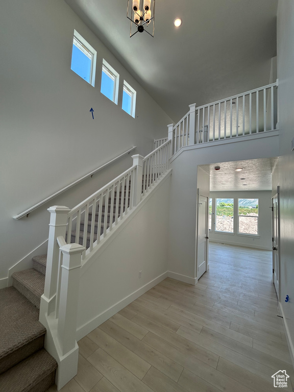Stairs with plenty of natural light, a towering ceiling, wood finished floors, a chandelier, and baseboards