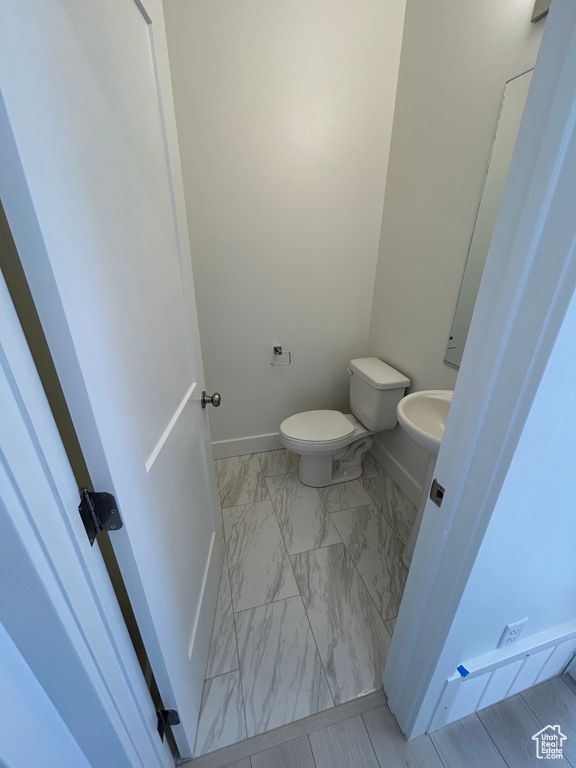 Half bath featuring marble look tile flooring, toilet, and baseboards