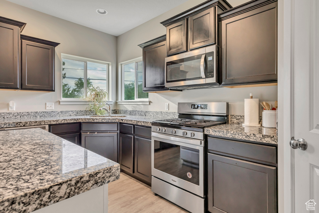 Kitchen with stainless steel appliances, light wood finished floors, dark brown cabinets, light stone countertops, and recessed lighting