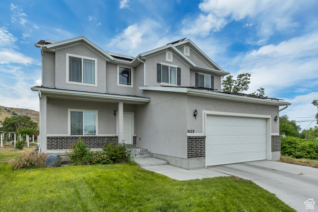 View of front of house with a front yard, solar panels, brick siding, and driveway