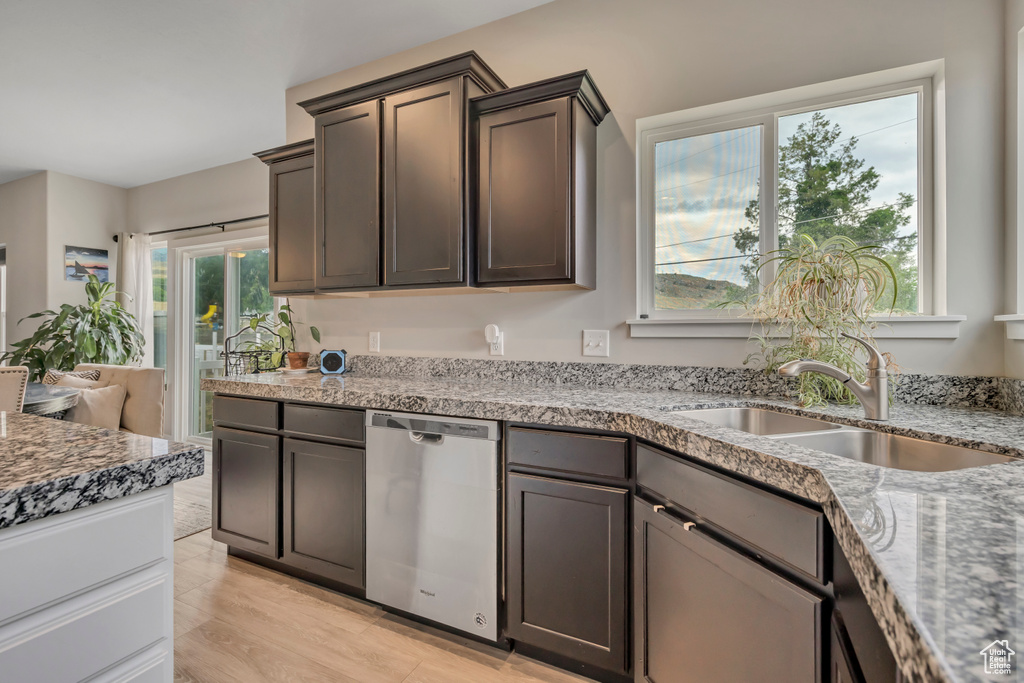 Kitchen with stainless steel dishwasher, light stone counters, and dark brown cabinetry
