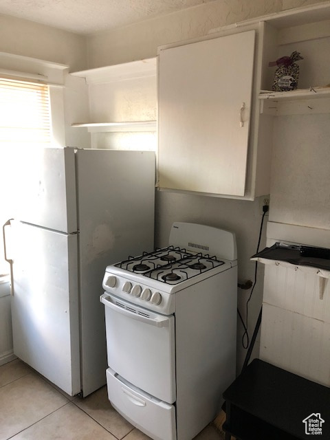 Kitchen featuring white appliances, light tile patterned flooring, open shelves, and white cabinetry