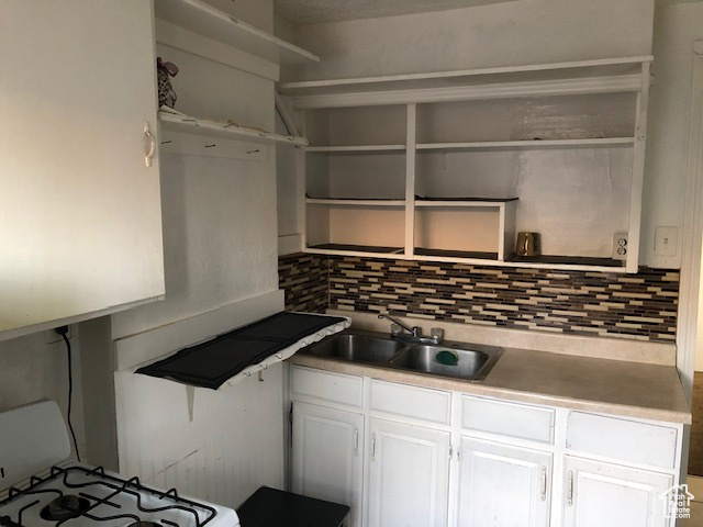 Kitchen with open shelves, a sink, tasteful backsplash, and white cabinets