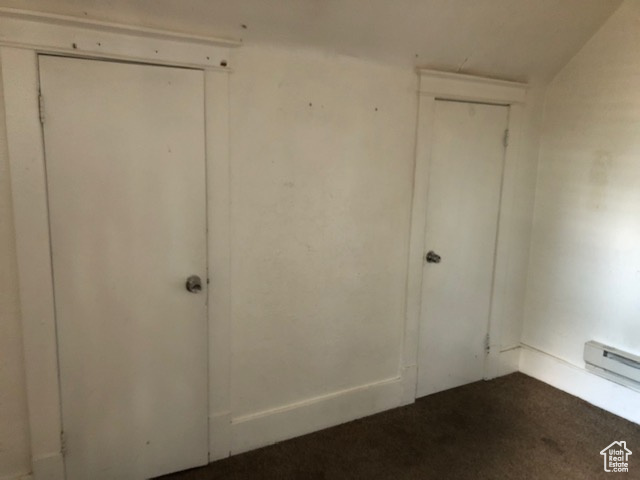 Unfurnished bedroom featuring dark colored carpet and a baseboard heating unit