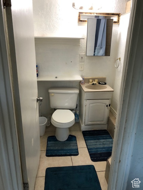 Bathroom with toilet, vanity, tile patterned flooring, and a textured wall
