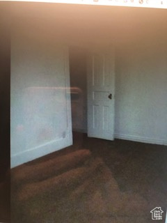 Unfurnished room featuring baseboards and dark carpet
