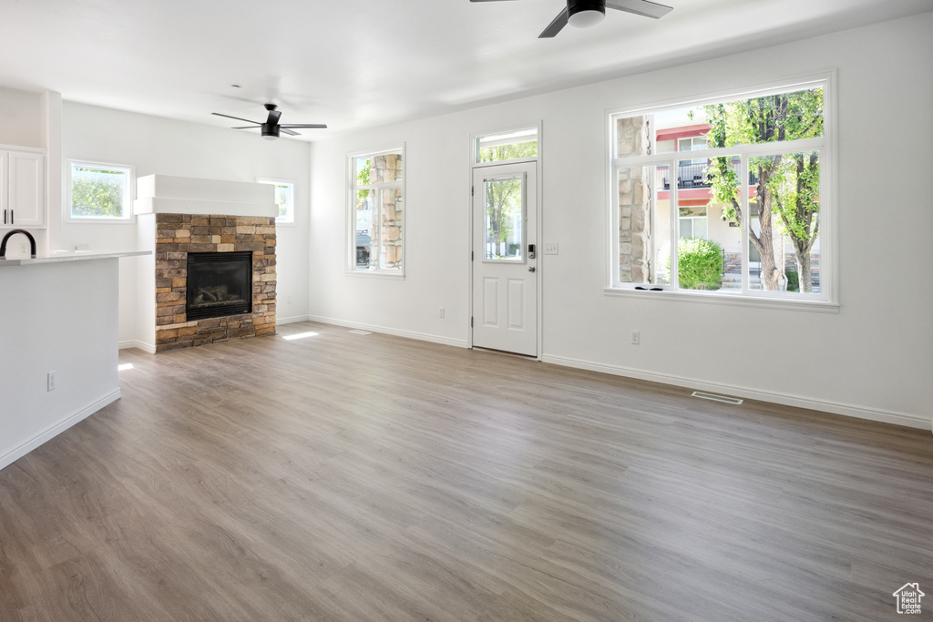 Unfurnished living room with ceiling fan, a stone fireplace, light wood-style floors, and baseboards