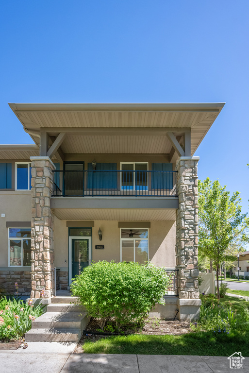 View of front facade featuring a balcony, stucco siding, stone siding, and covered porch