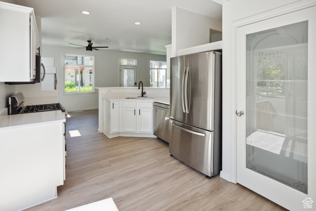 Kitchen featuring appliances with stainless steel finishes, a sink, a peninsula, ceiling fan, and white cabinetry