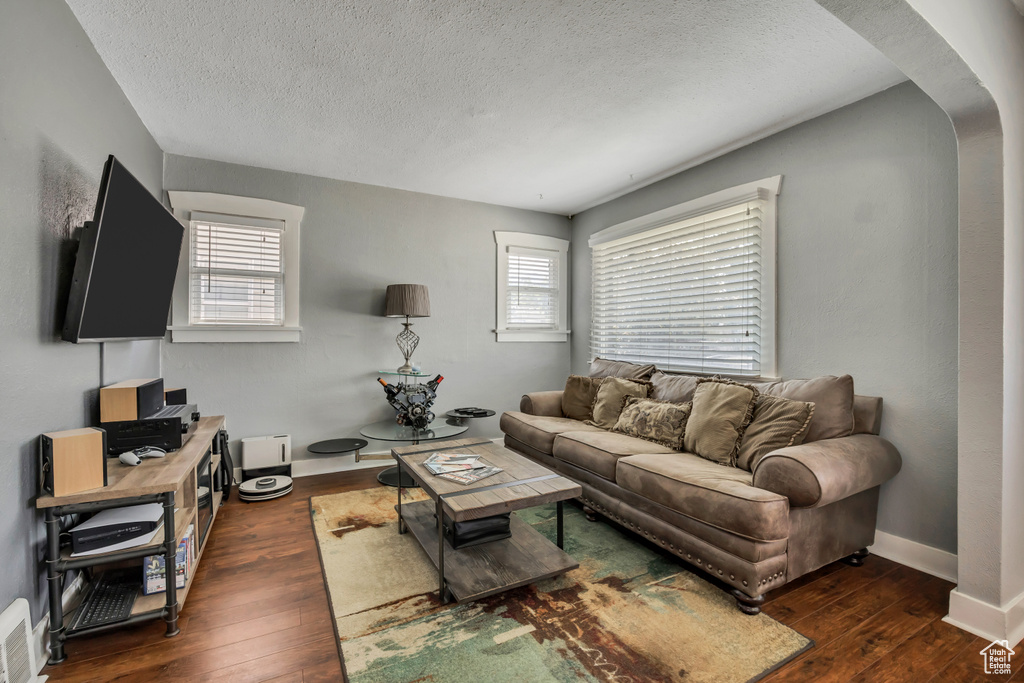 Living room featuring arched walkways, hardwood / wood-style flooring, a textured ceiling, and baseboards